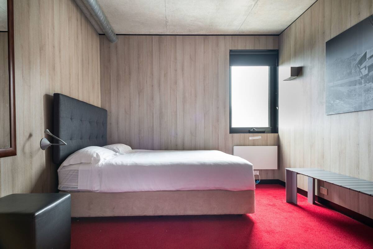 Une chambre d’hôtel comprenant un lit, une table de chevet, un banc, un téléviseur fixé au mur et une fenêtre.