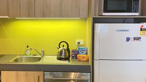 A kitchen with wooden cabinets, a stainless steel sink, a kettle, a microwave, and a refrigerator. - Buller Central (Mount Buller)