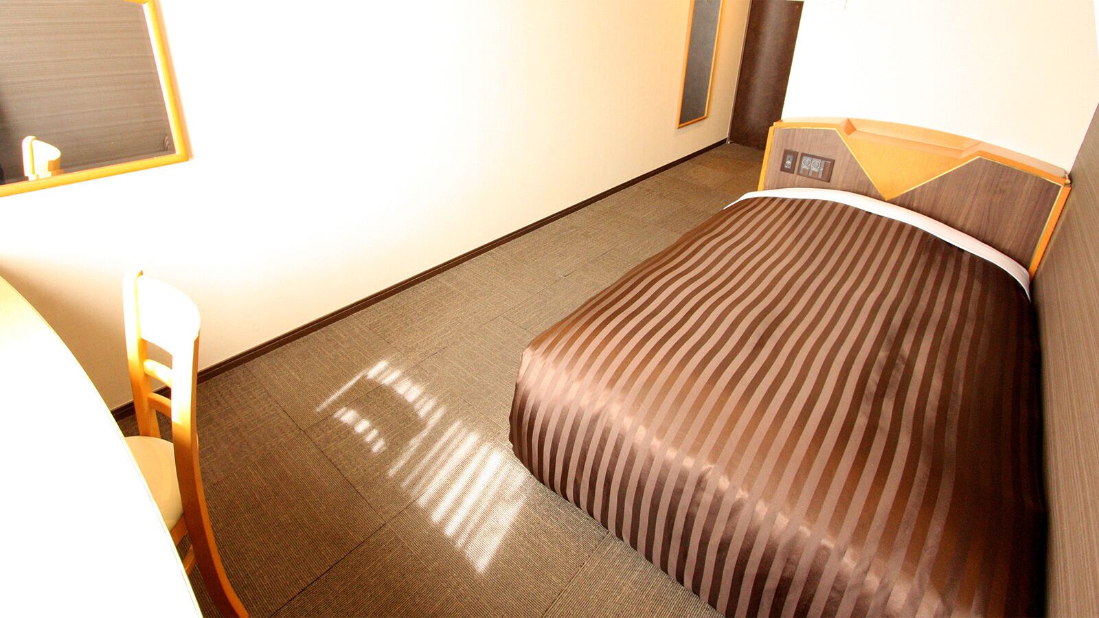 A hotel room with a bed, a chair, a desk, and a mirror.