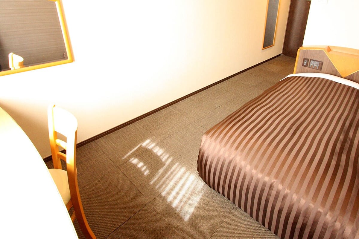 A hotel room with a bed, a chair, a desk, and a mirror.