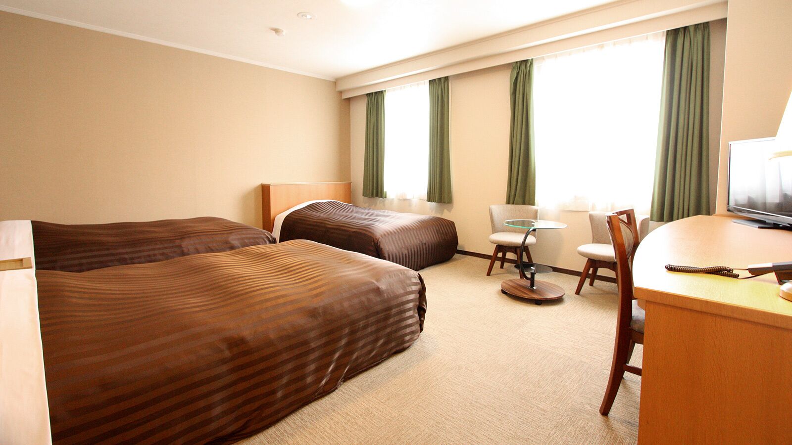 A hotel room with two beds, a desk, a chair, a small table, and a television.