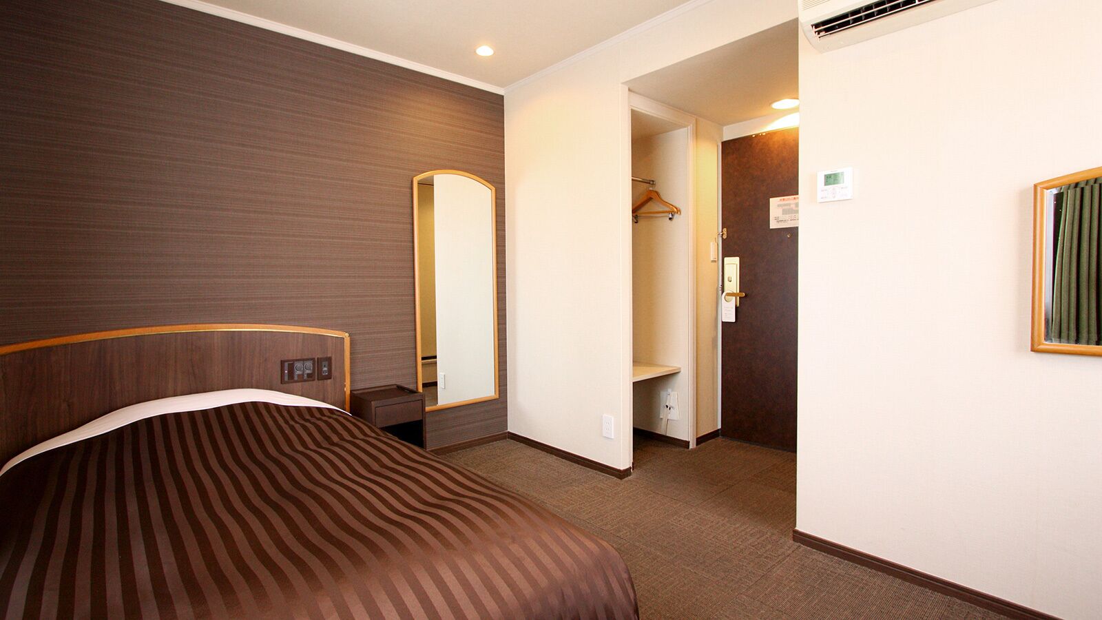 A hotel room with a bed, a mirror, a wardrobe, and a door leading to a bathroom.