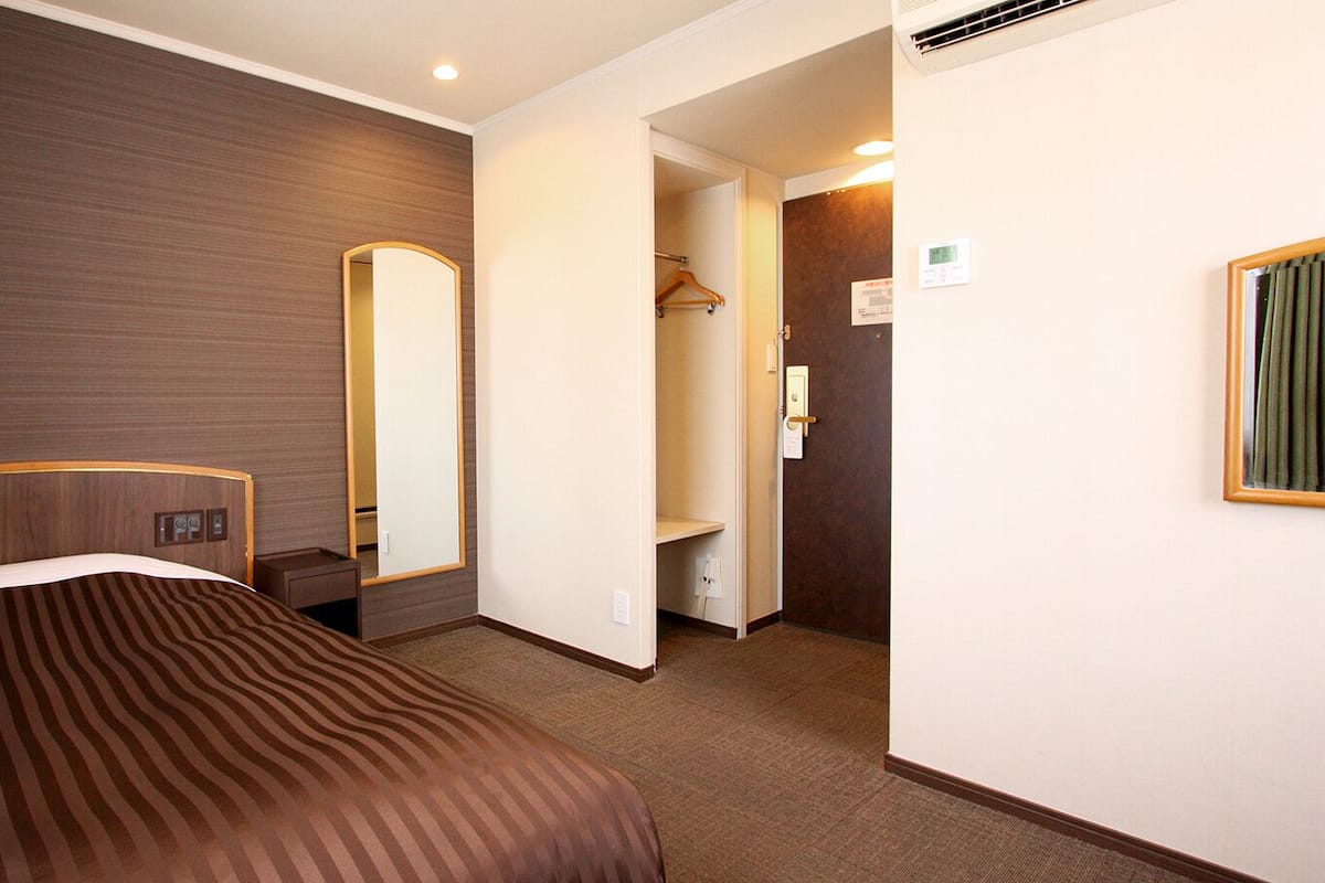A hotel room with a bed, a mirror, a wardrobe, and a door leading to a bathroom.