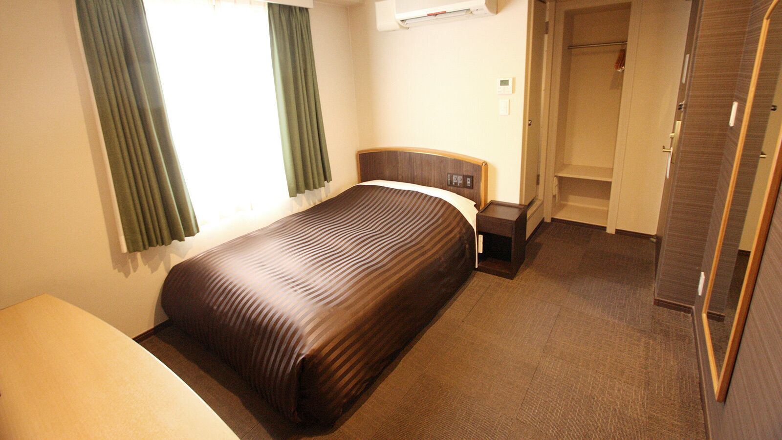 A hotel room with a bed, a bedside table, a wardrobe, and a bathroom door.