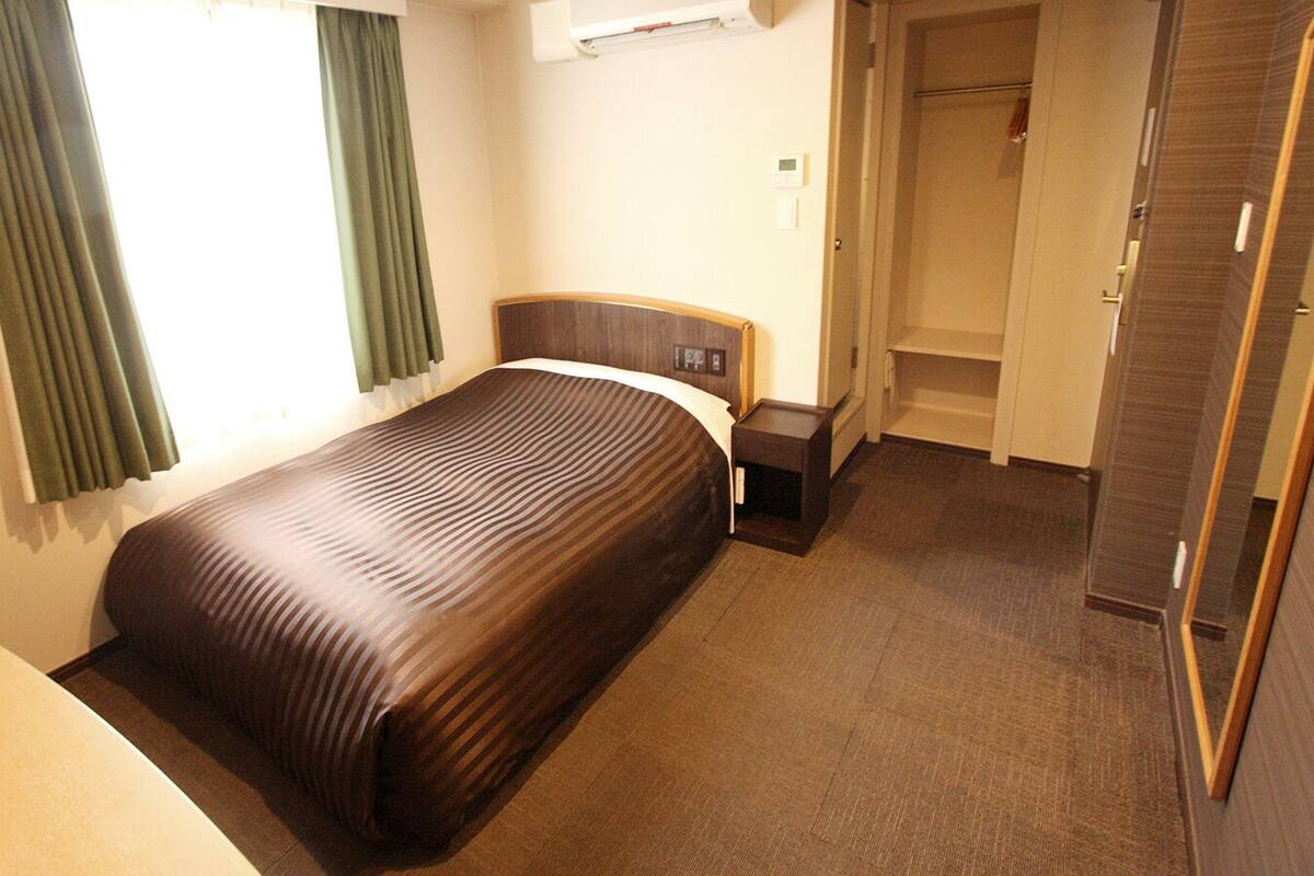 A hotel room with a bed, a bedside table, a wardrobe, and a bathroom door.
