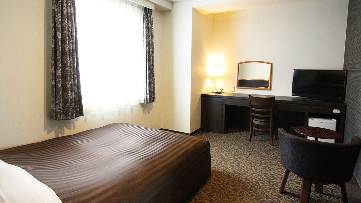 A hotel room with a bed, a desk with a chair, a television, and a mirror.