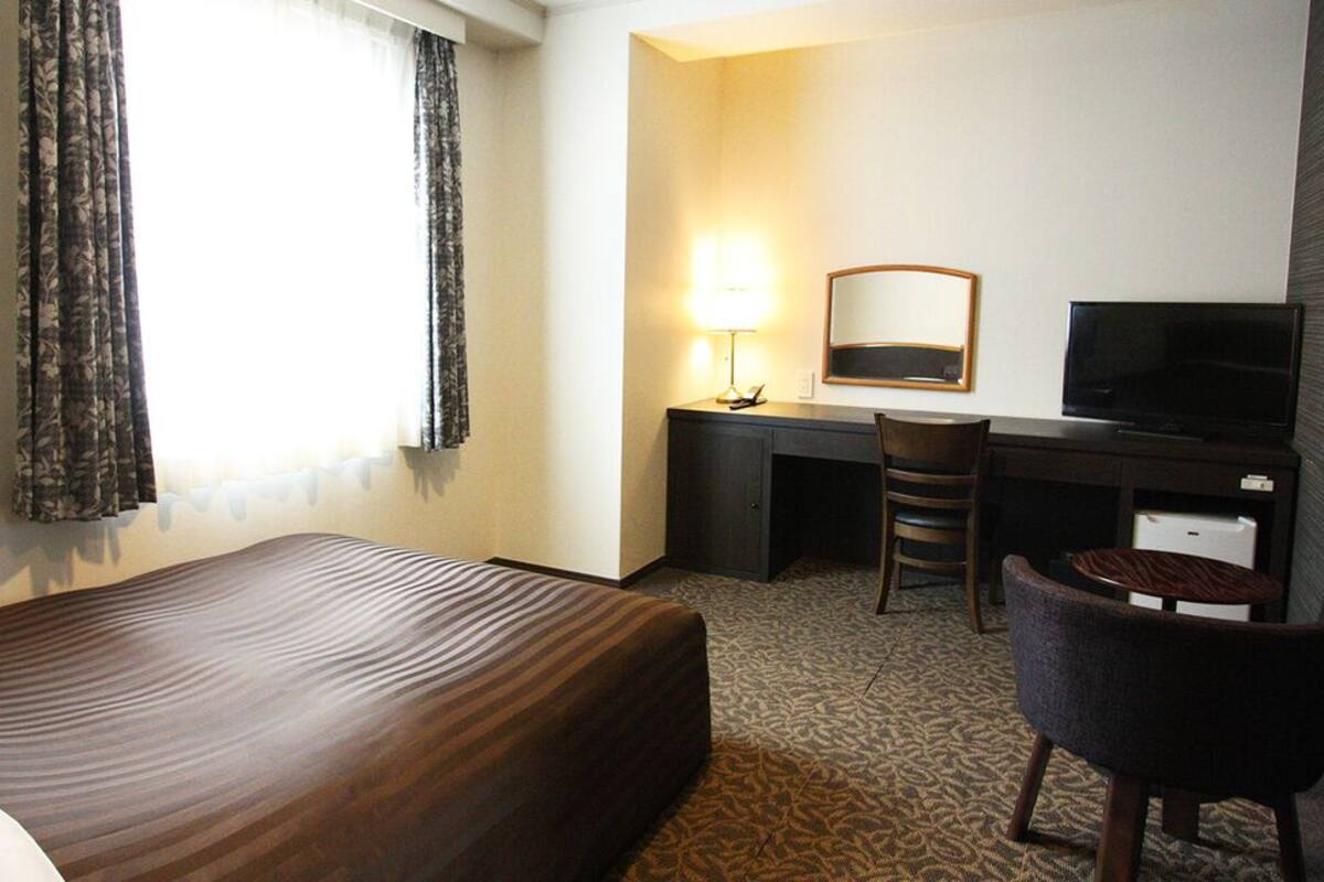 A hotel room with a bed, a desk with a chair, a television, and a mirror.