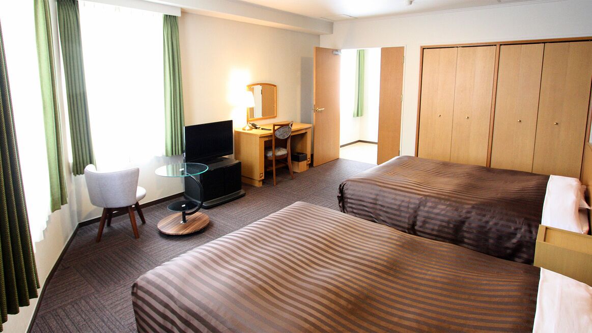 A hotel room with two beds, a desk with a chair, a television, and a wardrobe.