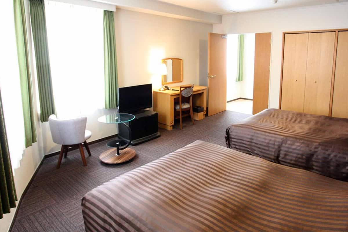 A hotel room with two beds, a desk with a chair, a television, and a wardrobe.