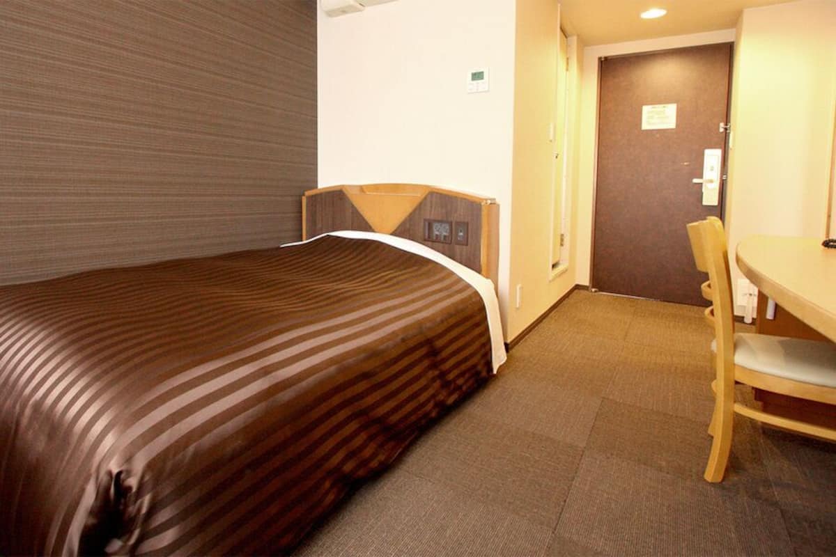 A hotel room with a bed, a desk, and a chair.
