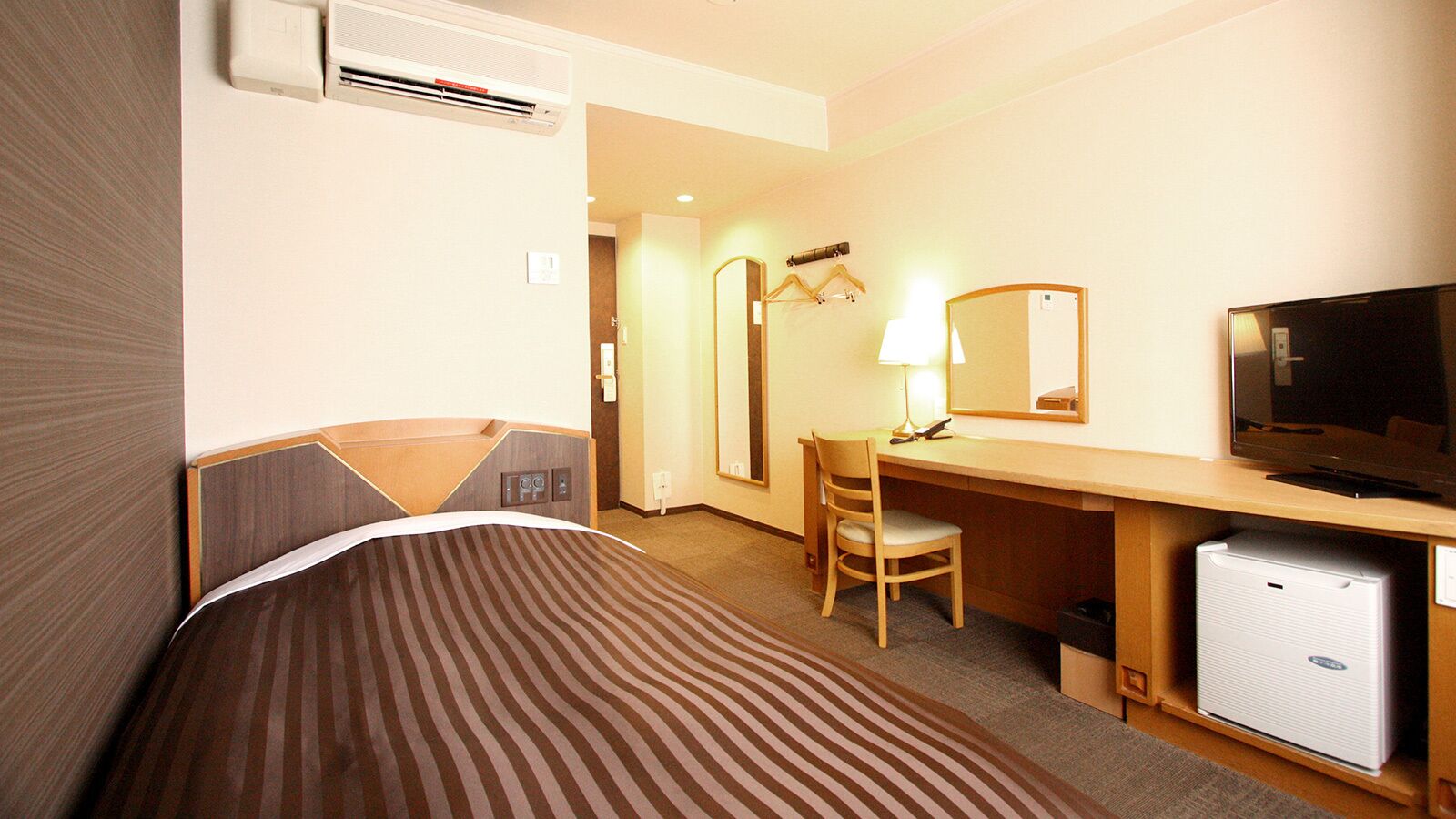 A hotel room with a bed, a desk, a chair, a television, and a mini-fridge.