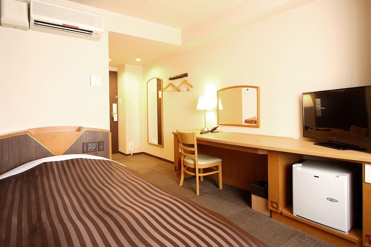 A hotel room with a bed, a desk, a chair, a television, and a mini-fridge.