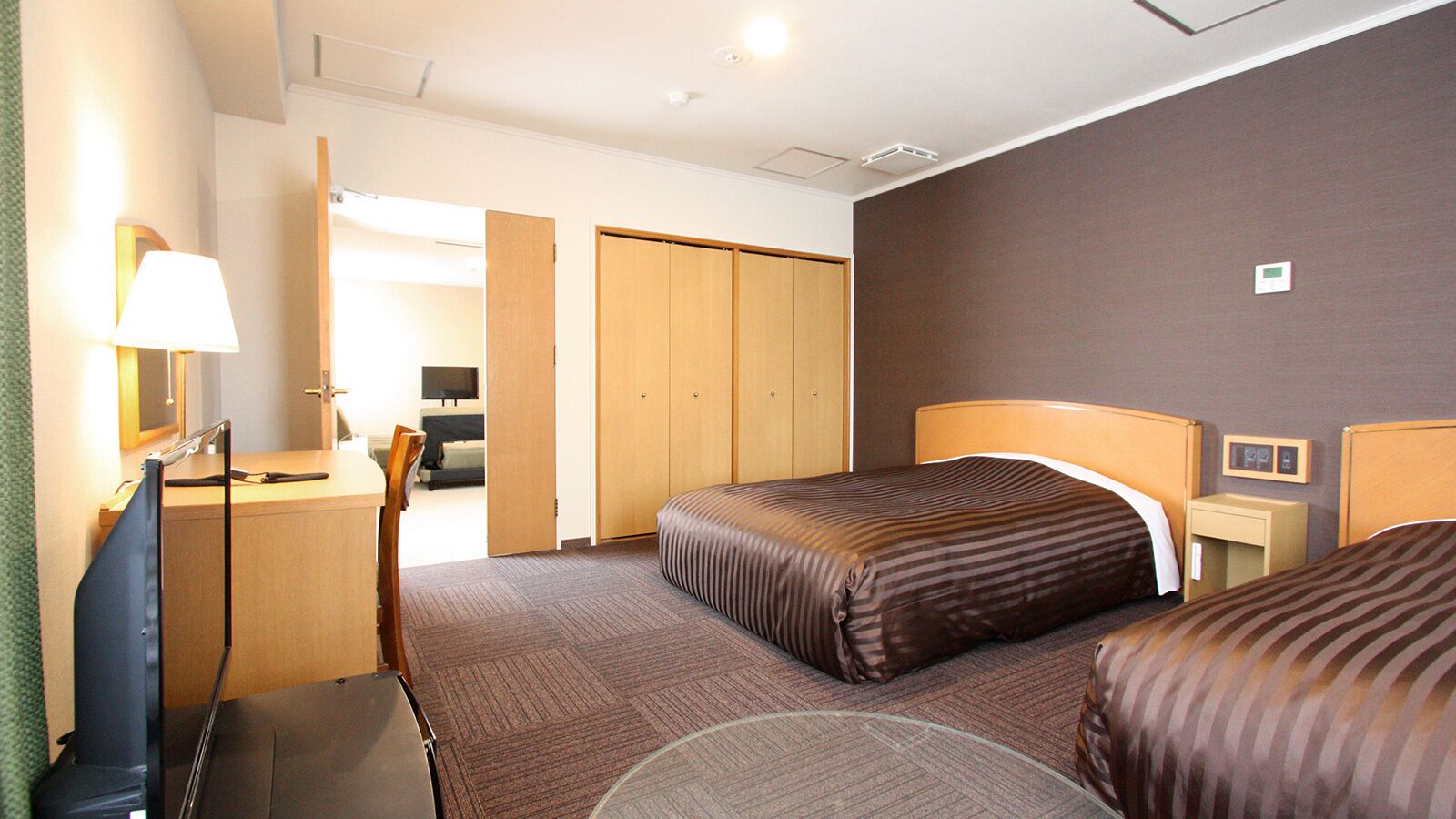 A hotel room with two beds, a desk, a chair, a lamp, and a wardrobe.