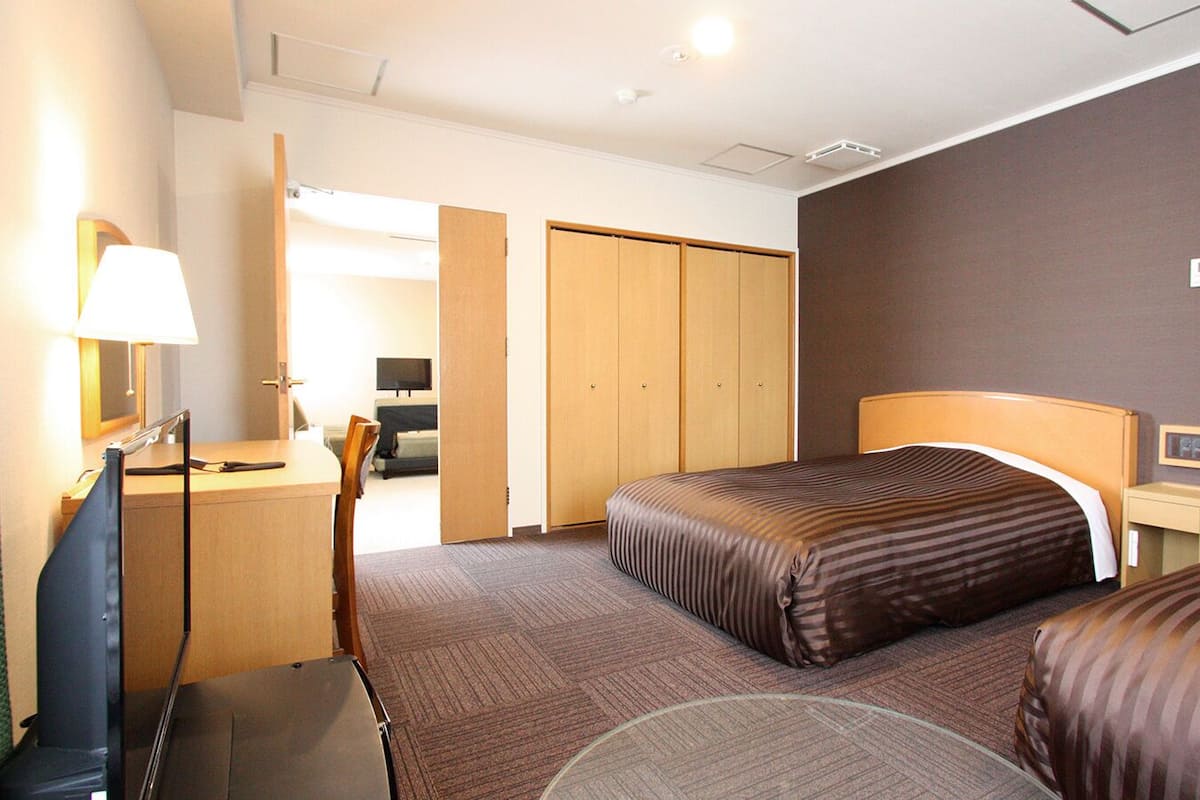 A hotel room with two beds, a desk, a chair, a lamp, and a wardrobe.