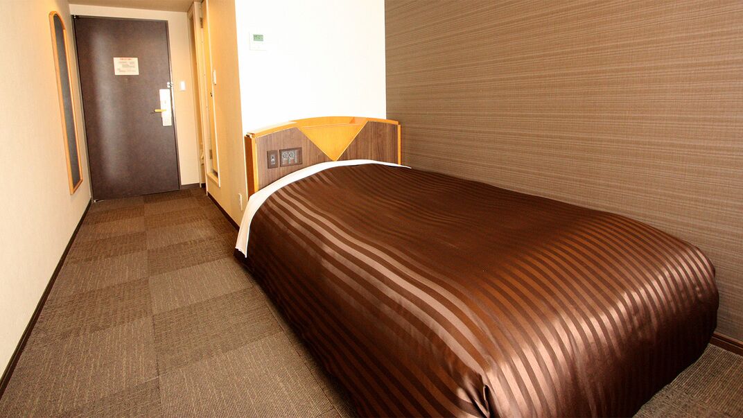 A hotel room with a bed, a door, and a carpeted floor.