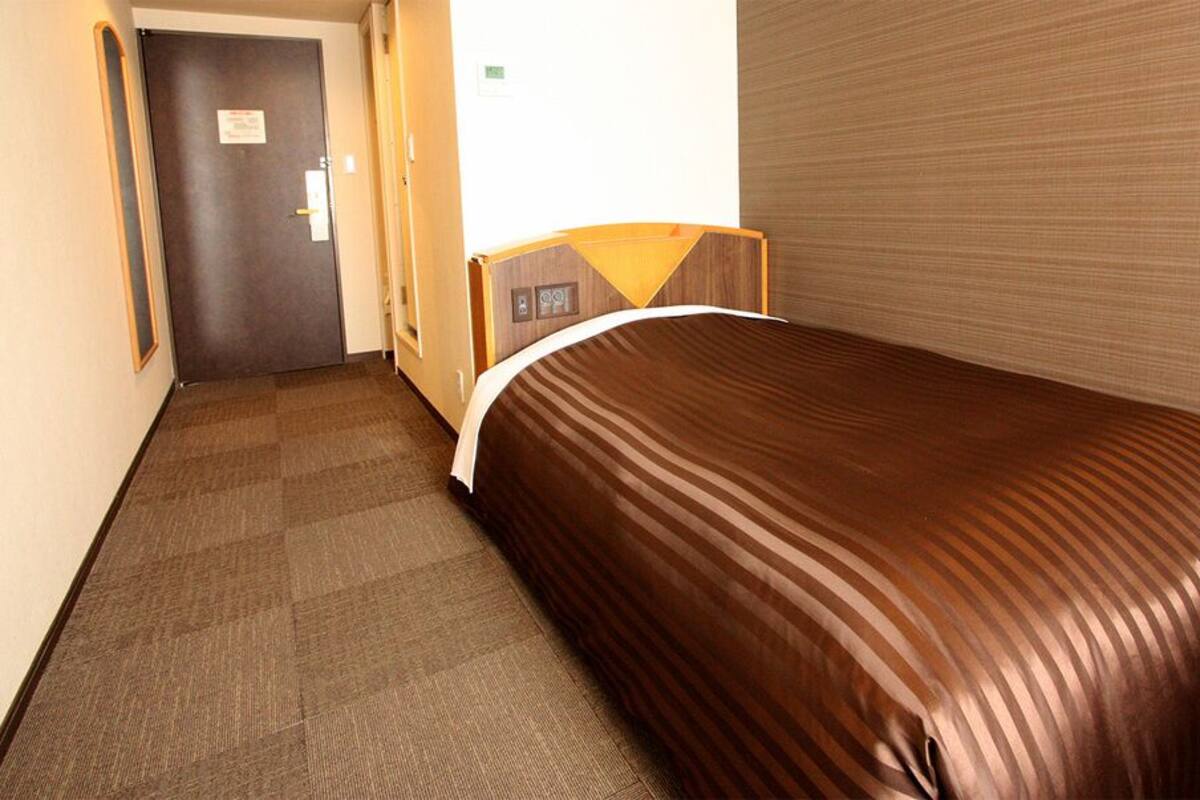 A hotel room with a bed, a door, and a carpeted floor.