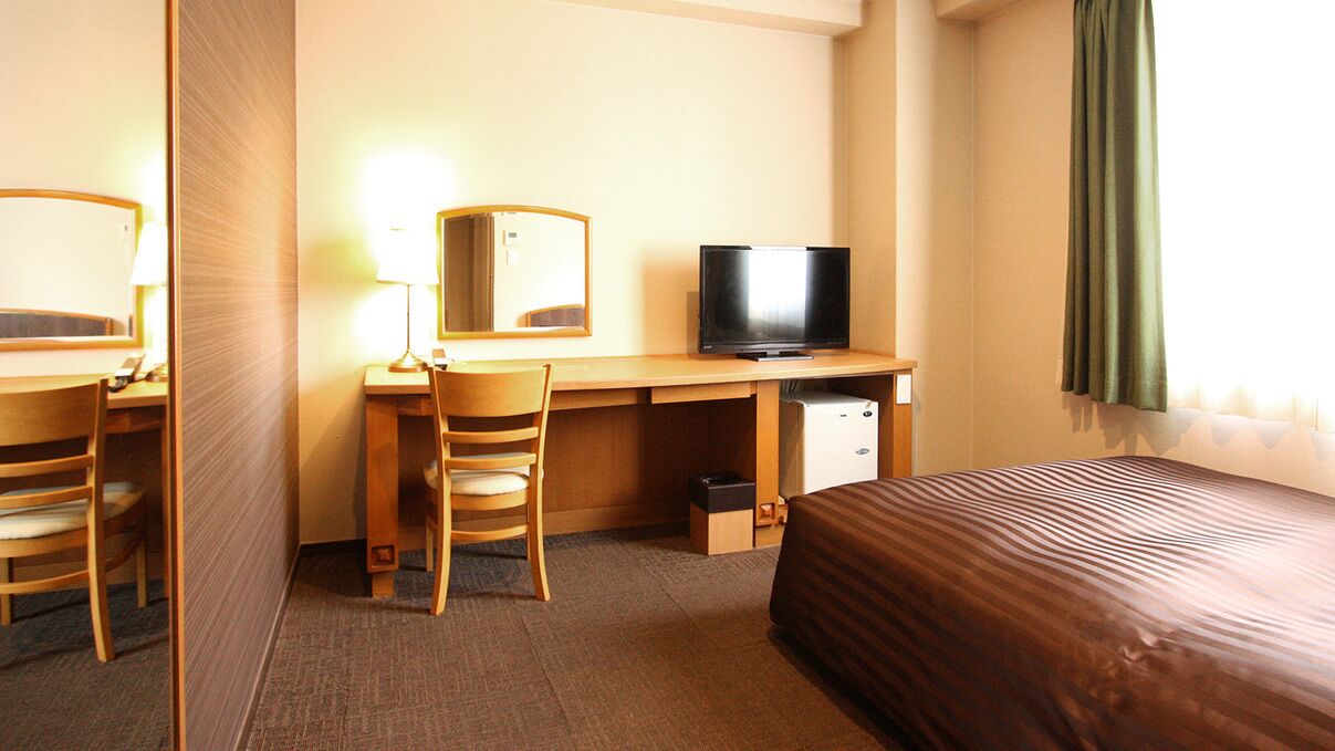 A hotel room with a bed, a desk with a chair, a television, and a mirror.