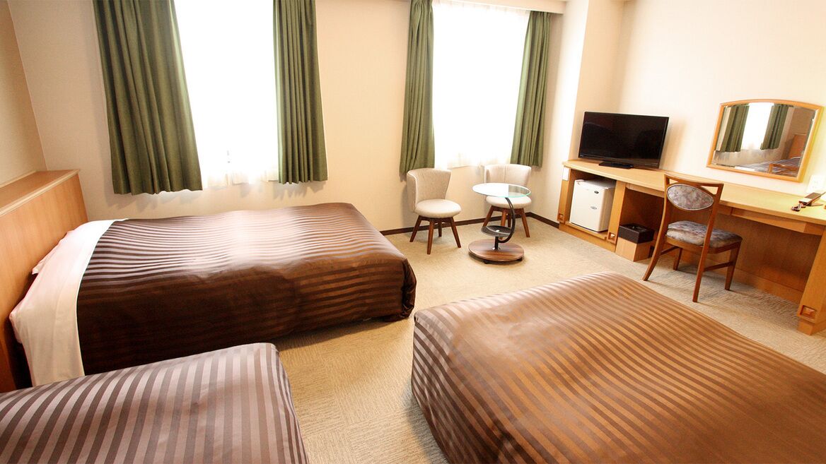A hotel room with two beds, a desk with a TV, a chair, and a small table.