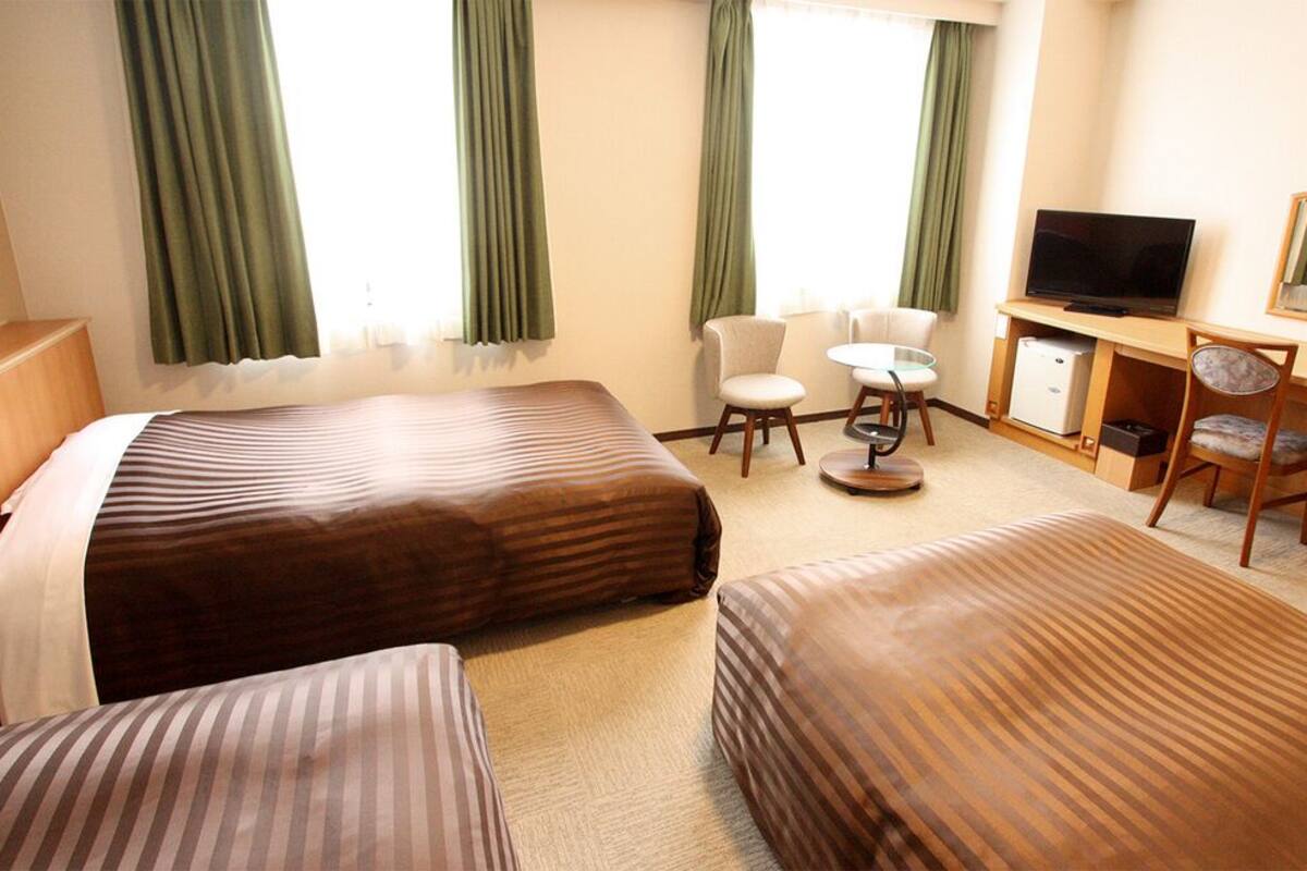 A hotel room with two beds, a desk with a TV, a chair, and a small table.