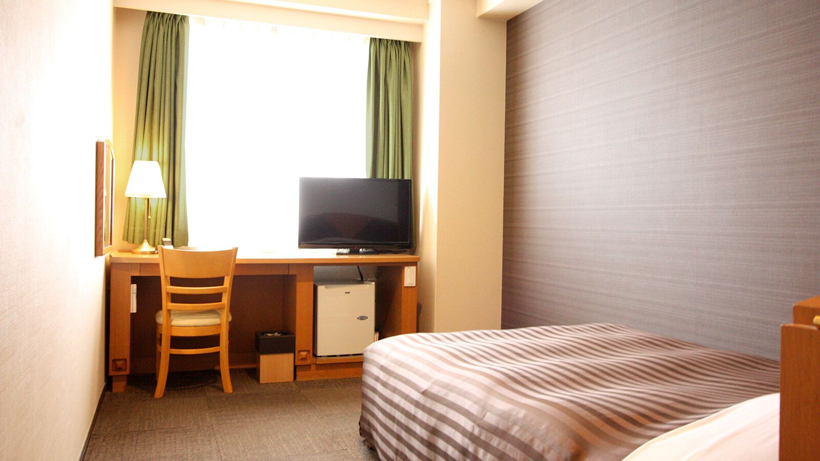 A hotel room with a bed, a desk with a television, a chair, and a small refrigerator.