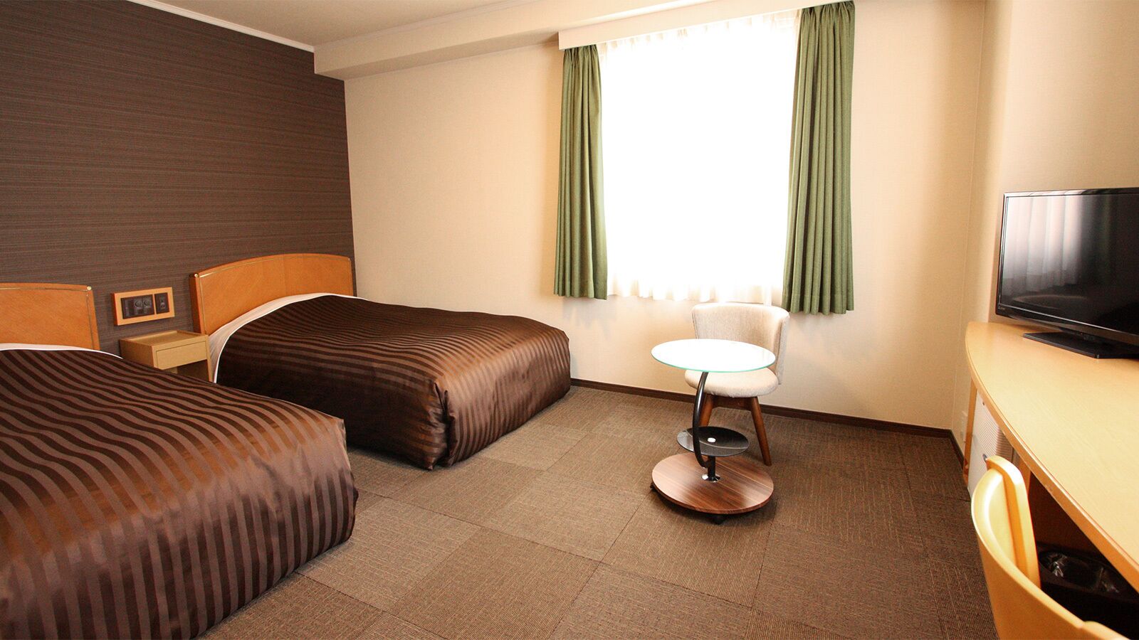 A hotel room with two beds, a small round table, a television, and a window with curtains.