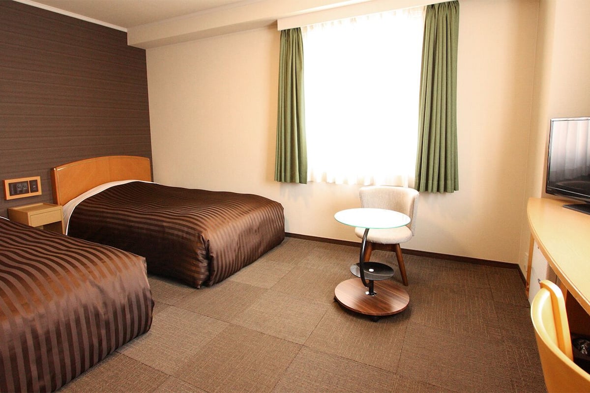 A hotel room with two beds, a small round table, a television, and a window with curtains.