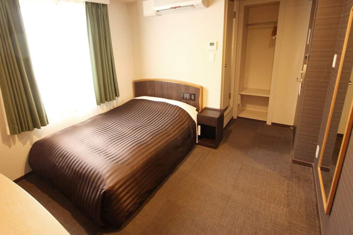A hotel room with a bed, a nightstand, a wardrobe, and a window with curtains.
