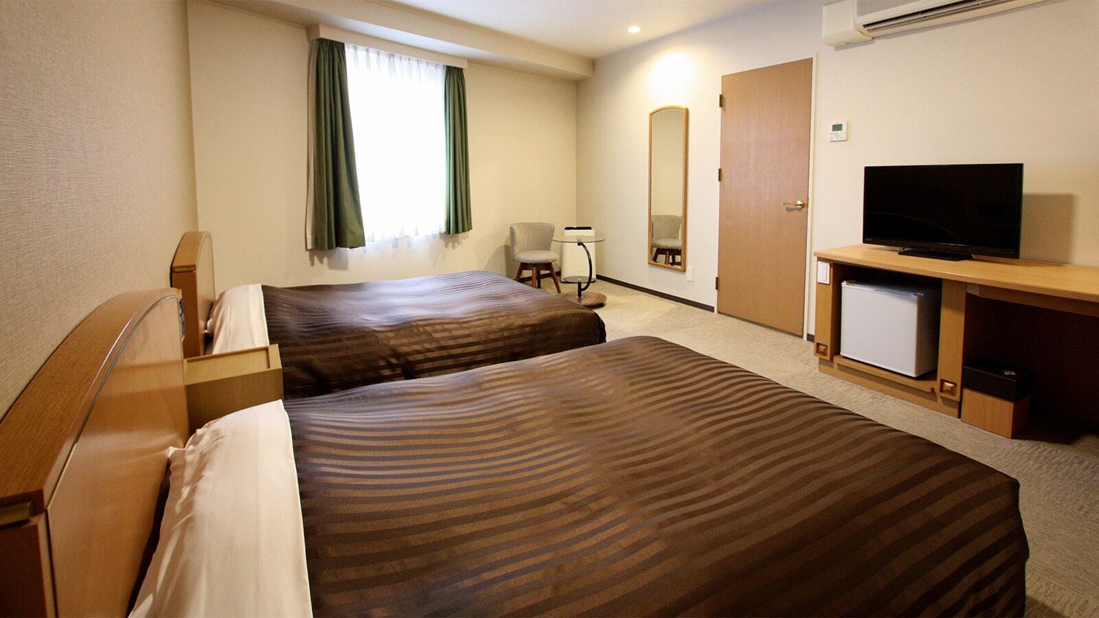 A hotel room with two beds, a TV, a desk, a chair, a mirror, and a window with curtains.