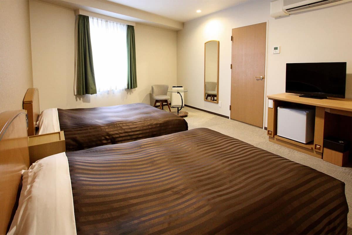 A hotel room with two beds, a TV, a desk, a chair, a mirror, and a window with curtains.