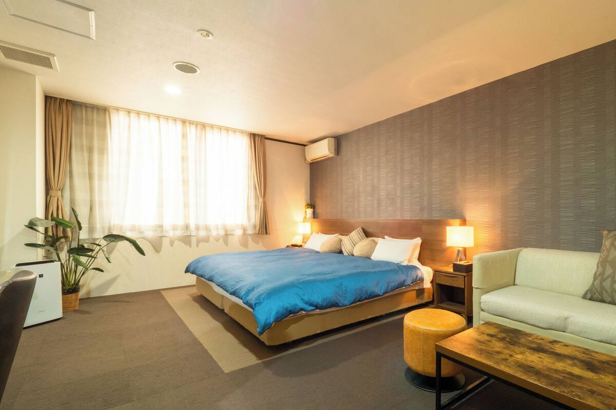 A hotel room with a bed, a sofa, a small table, and a potted plant.