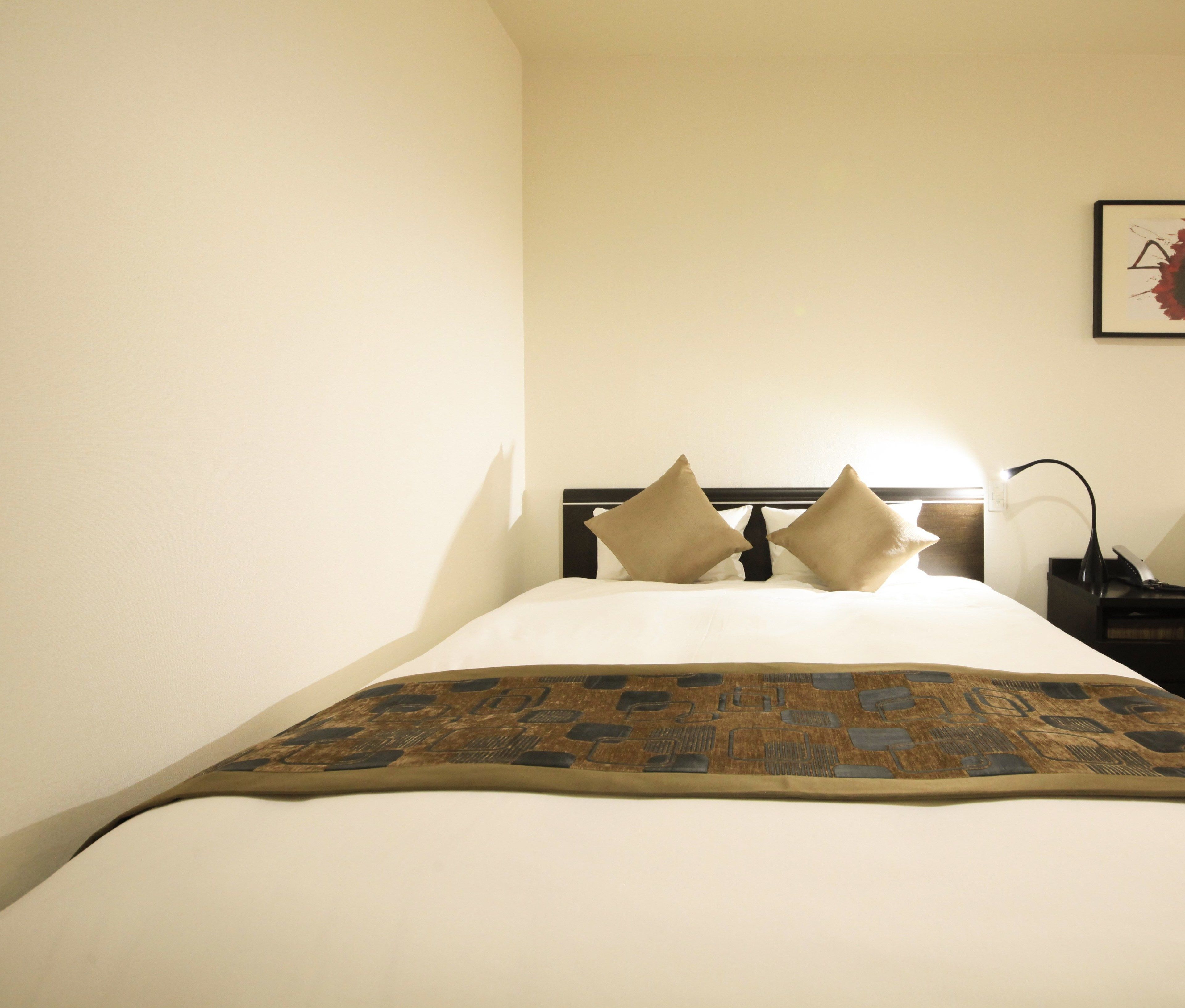 Una cama bien hecha con una colcha estampada, cabecera con dos almohadas y una mesita de noche con una lámpara y un teléfono.