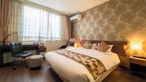 Habitación de hotel con cama, escritorio, silla, sillón de masaje y lámpara.