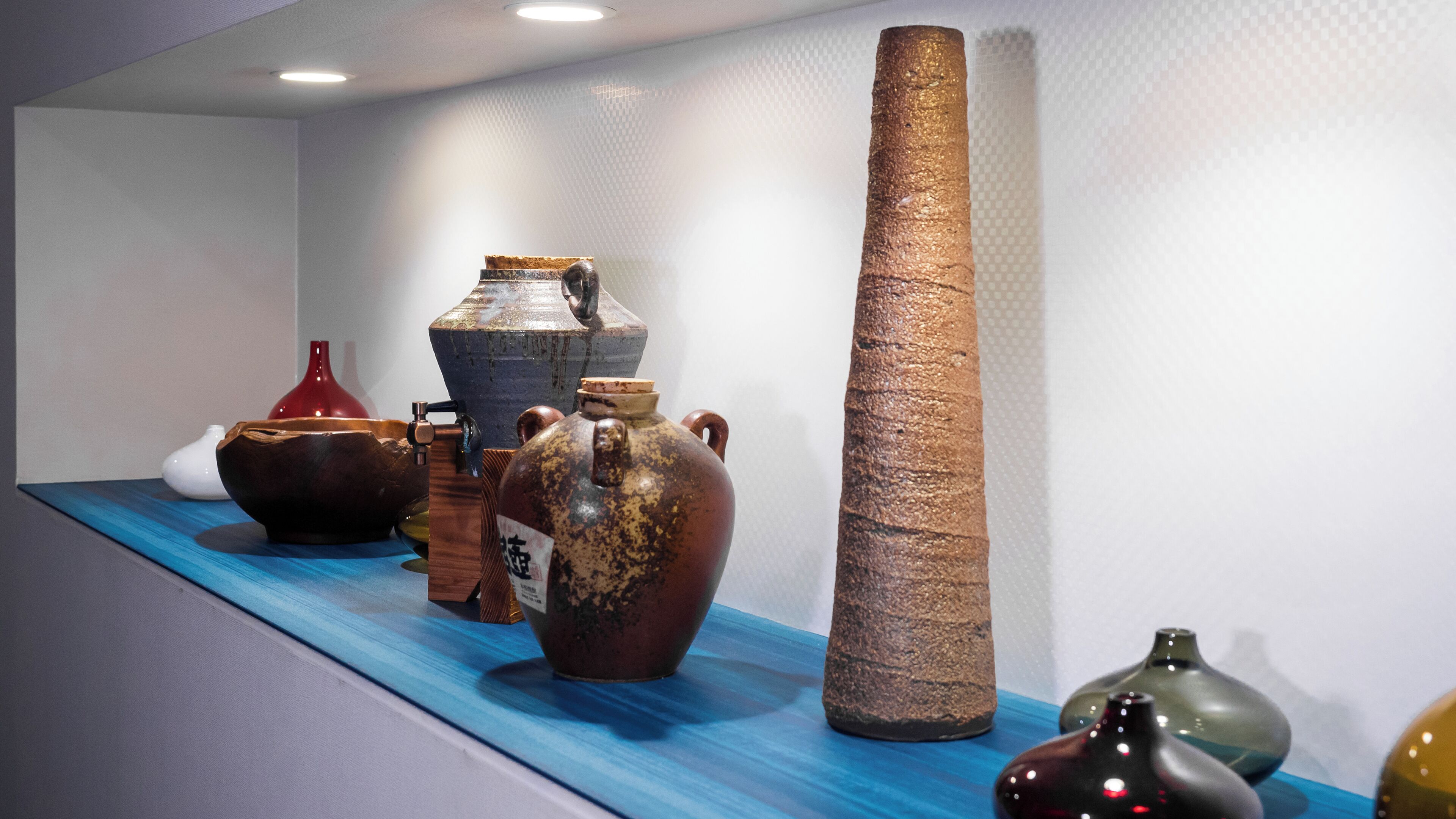 A display of various pottery items on a blue surface against a white wall.