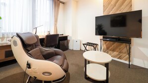 A hotel room with a massage chair, a desk with a computer, a flat-screen TV, and a small table. - Hotel Tohkai (Atsugi)