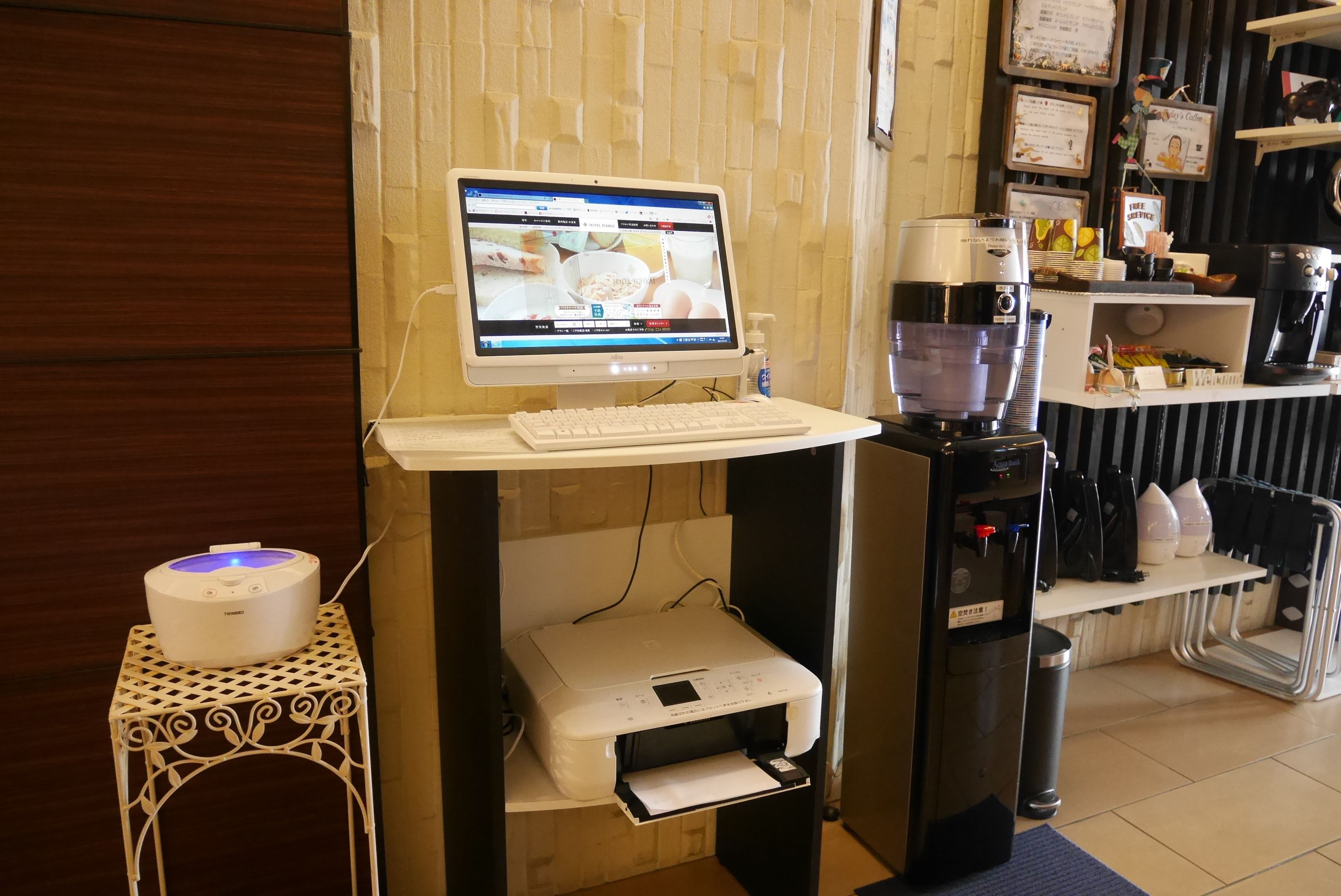 A coffee station with a computer monitor, keyboard, and coffee maker.