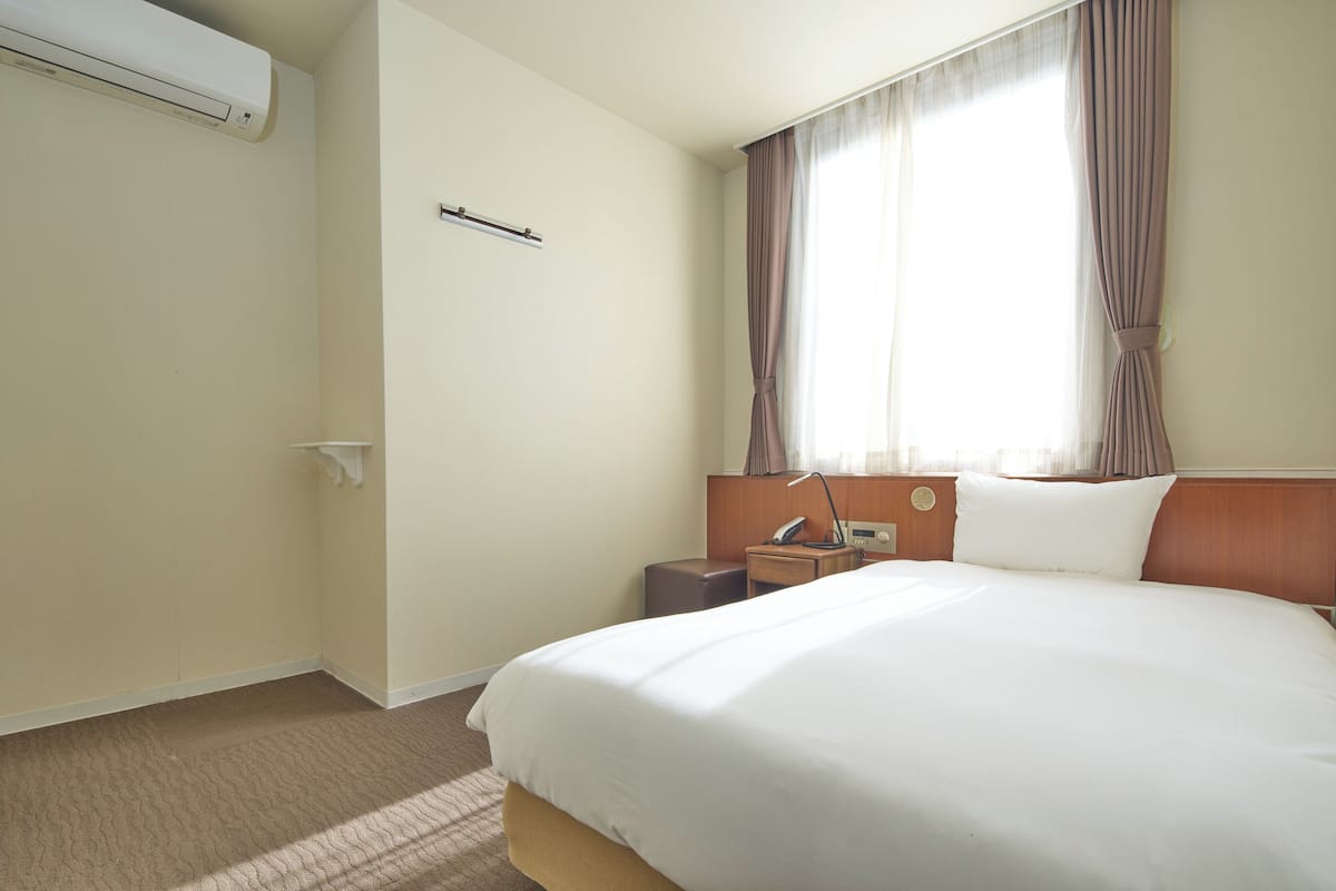 A hotel room with a large bed, a nightstand, a lamp, and a window with curtains.