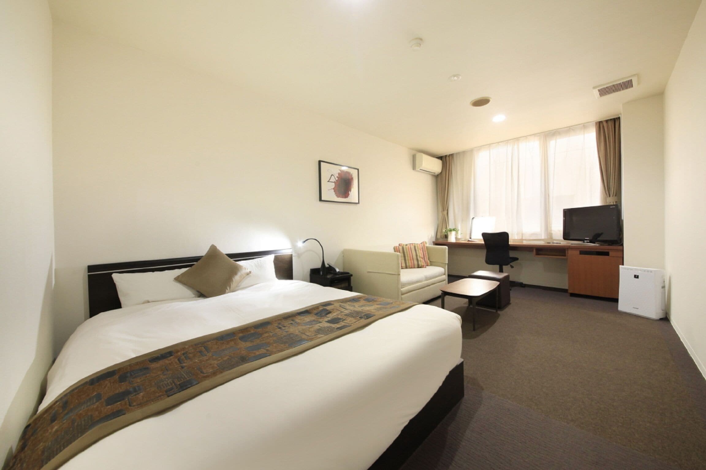A hotel room with a large bed, a desk, a chair, a sofa, a television, and a window with curtains.