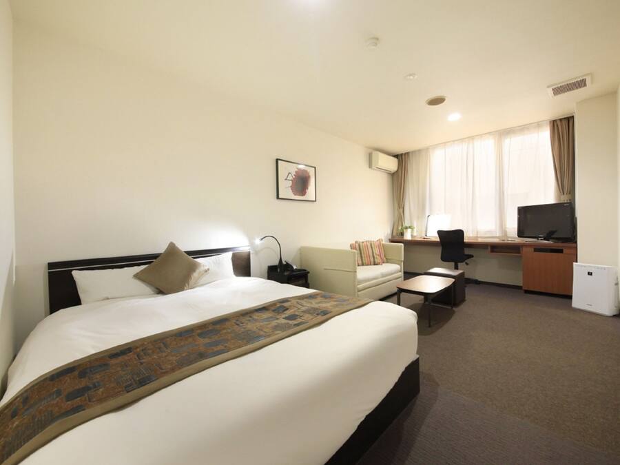A hotel room with a large bed, a desk, a chair, a sofa, a television, and a window with curtains.