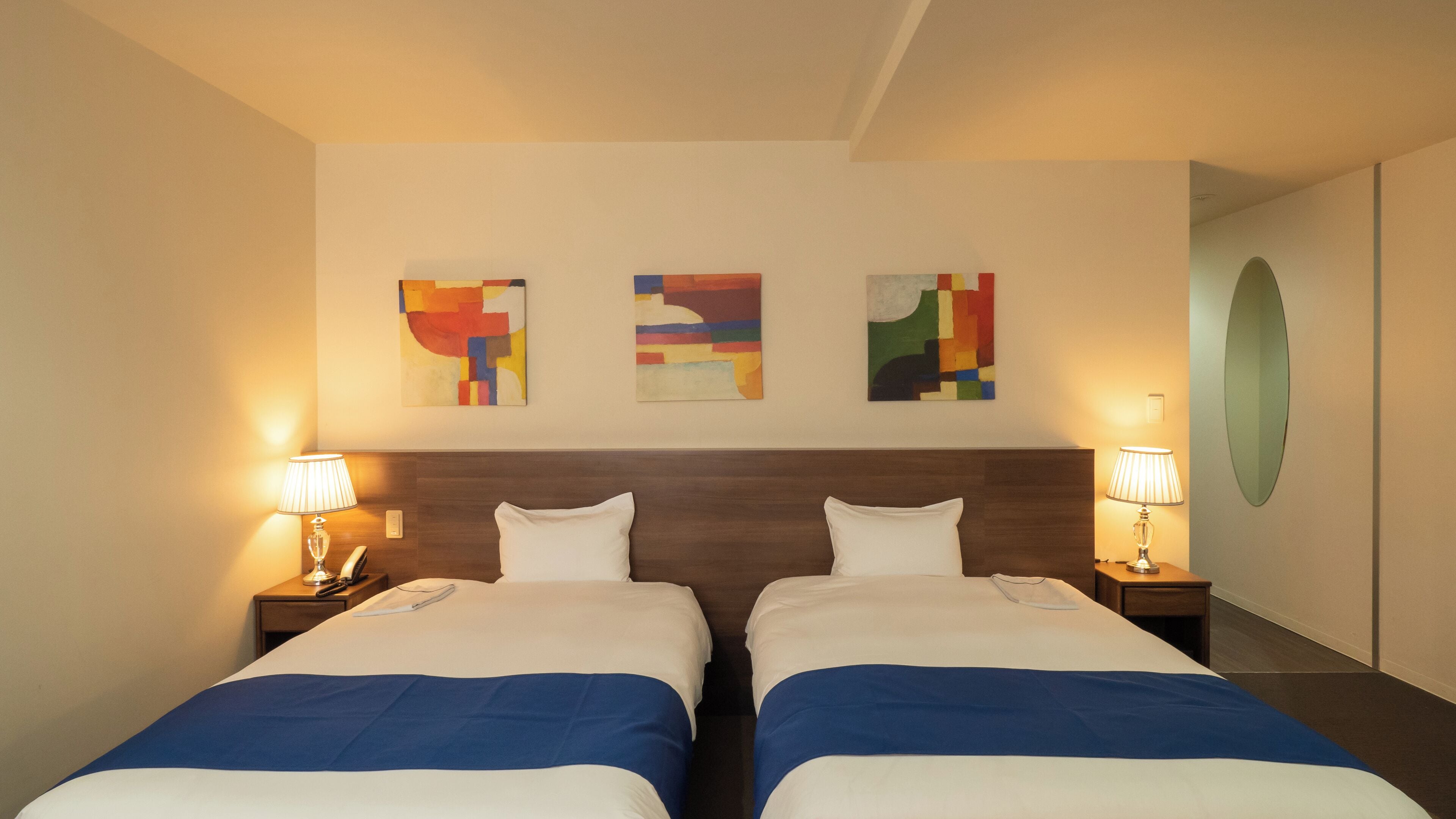 Ett hotellrum med två sängar, en sänggavel i trä och tre abstrakta målningar på väggen.