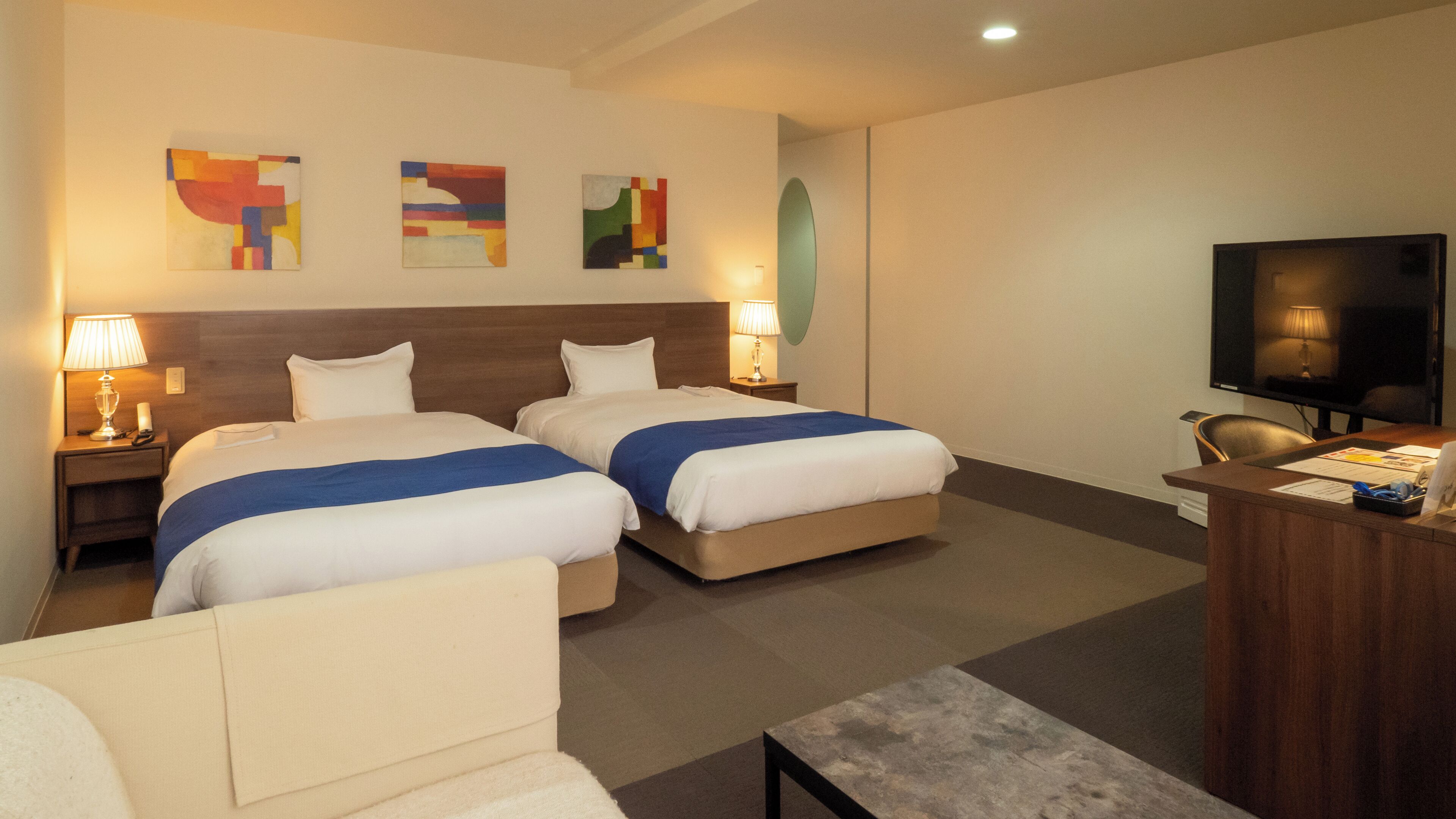 Une chambre d’hôtel avec deux lits, un bureau, une télévision et une œuvre d’art abstrait au mur.