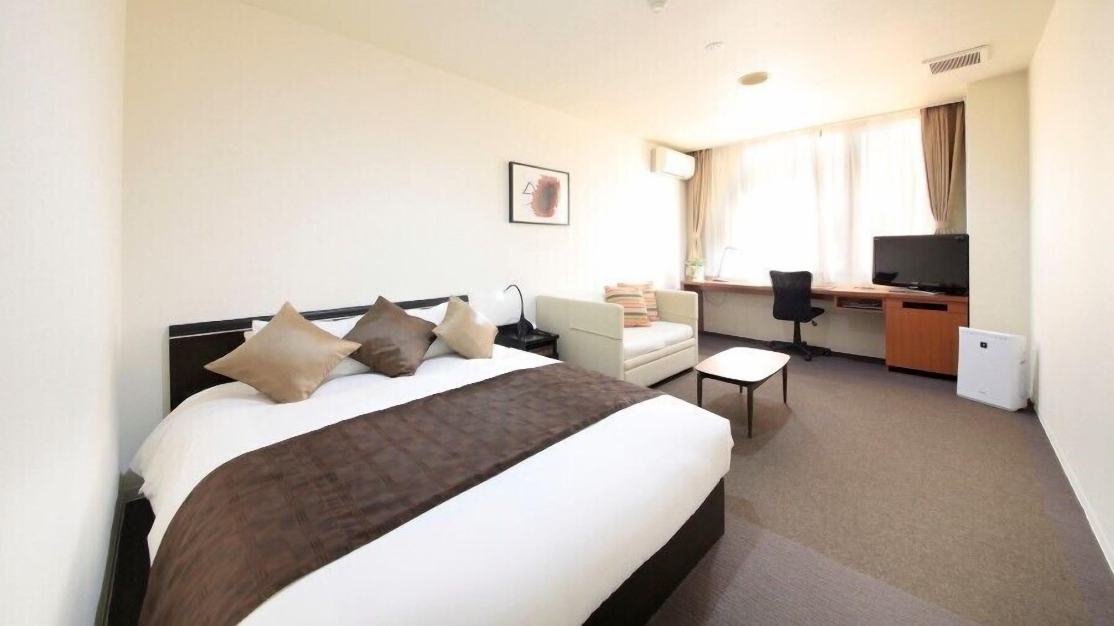 A hotel room with a bed, a desk, a chair, a television, and a window with curtains.