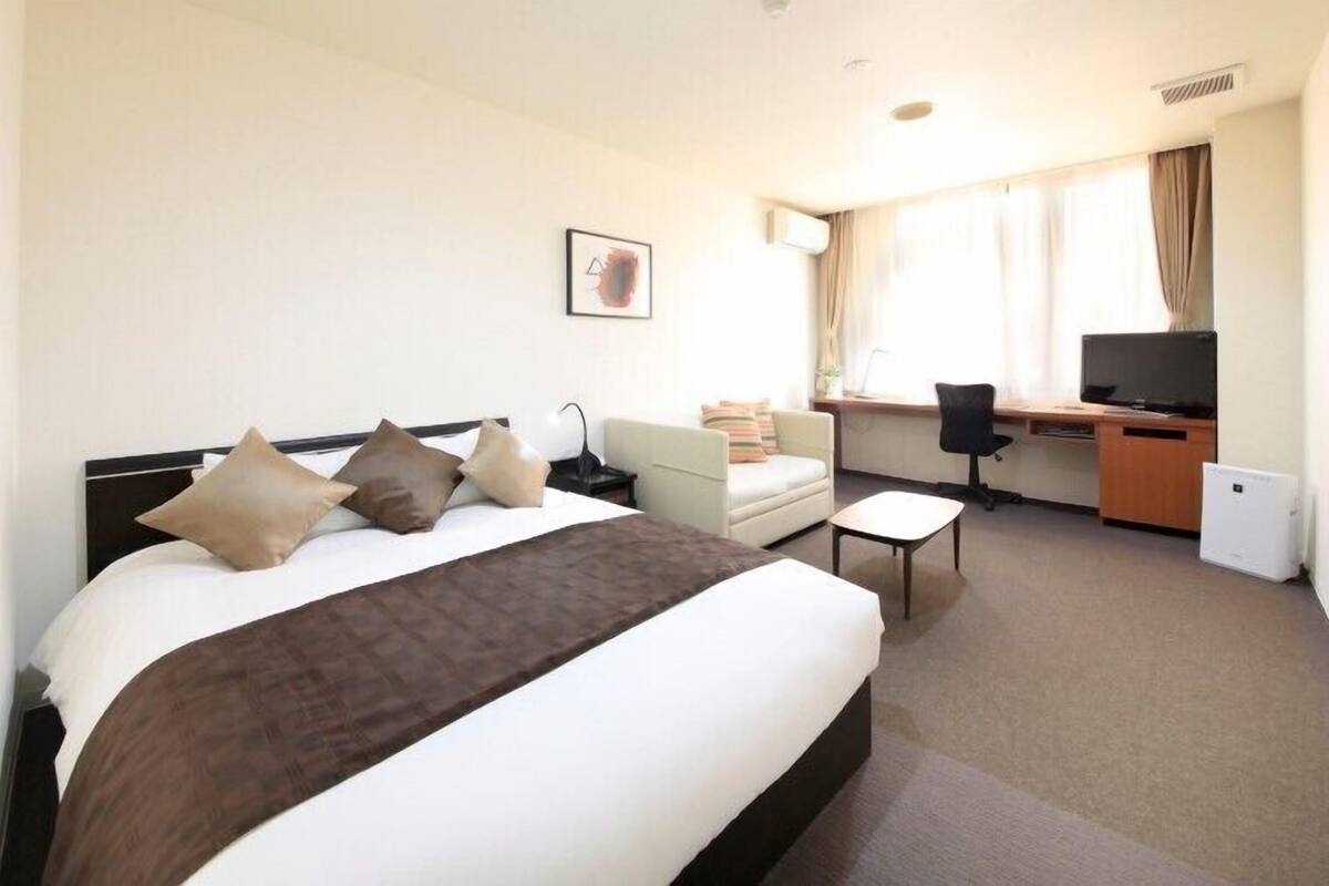 A hotel room with a bed, a desk, a chair, a television, and a window with curtains.