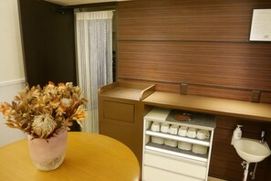 Una cocina compacta con una mesa de madera, un jarrón de flores secas, un refrigerador y un lavamanos.