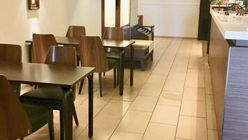 A modern dining area with wooden tables and chairs, a staircase, and a reception desk.