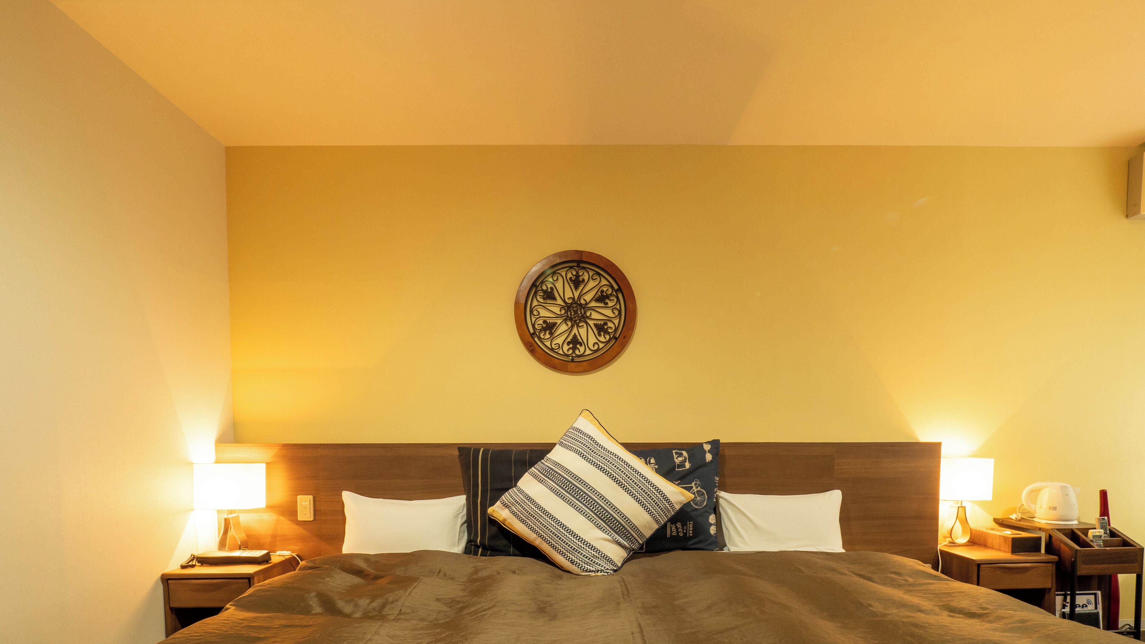 A hotel room with a bed, two bedside tables, a wall clock, and a lamp on each side.