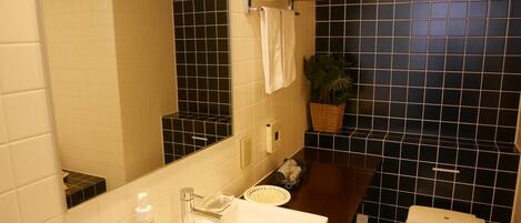 Un baño con lavamanos blanco, un espejo, toallero, planta en maceta y un inodoro.