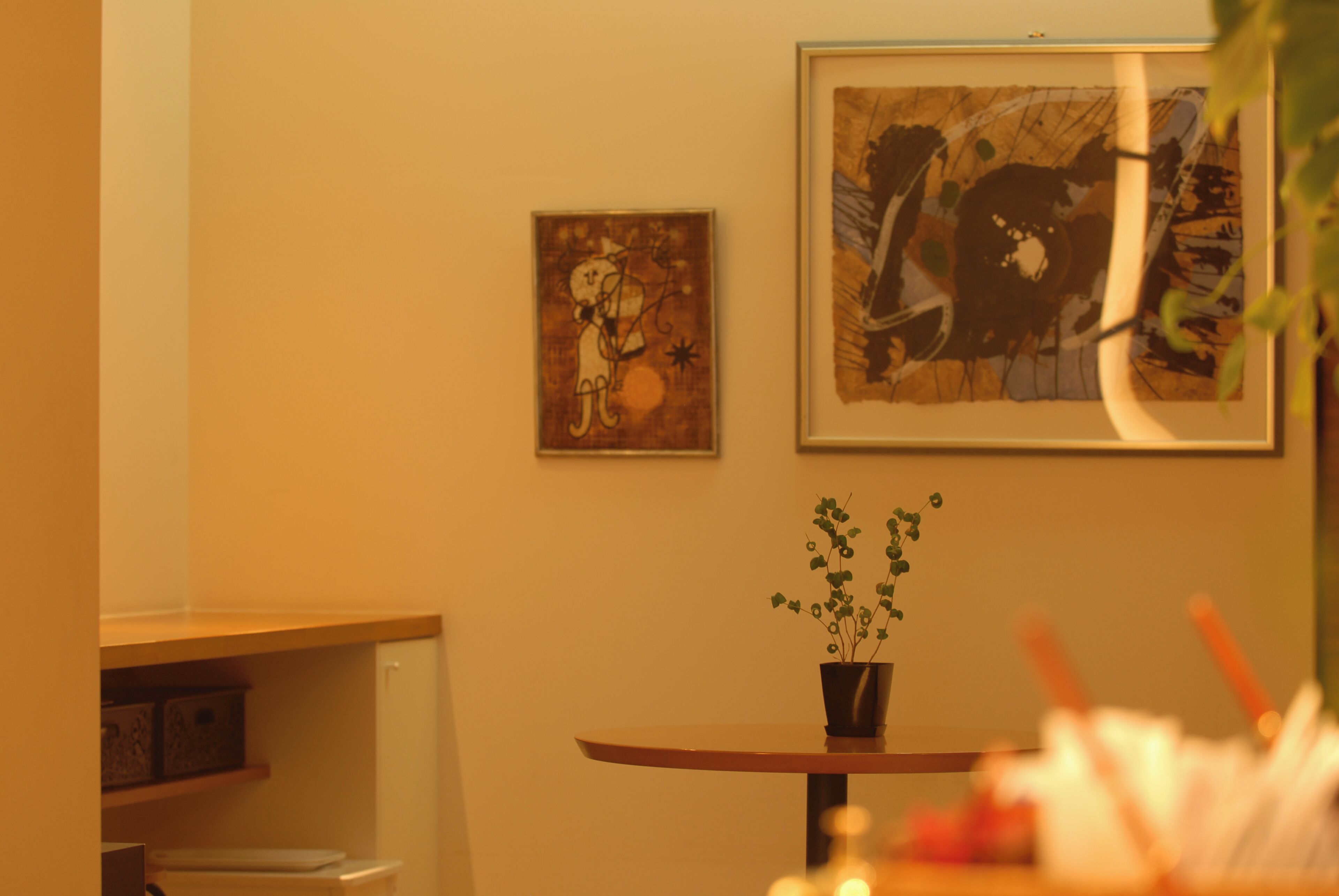 A room with a round table, a potted plant, and two framed artworks on the wall.