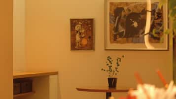 A room with a round table, a potted plant, and two framed artworks on the wall.