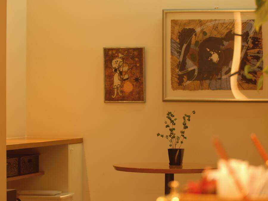 A room with a round table, a potted plant, and two framed artworks on the wall.