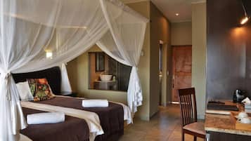 A hotel room with a bed, a small table, a chair, and a bathroom visible in the background.